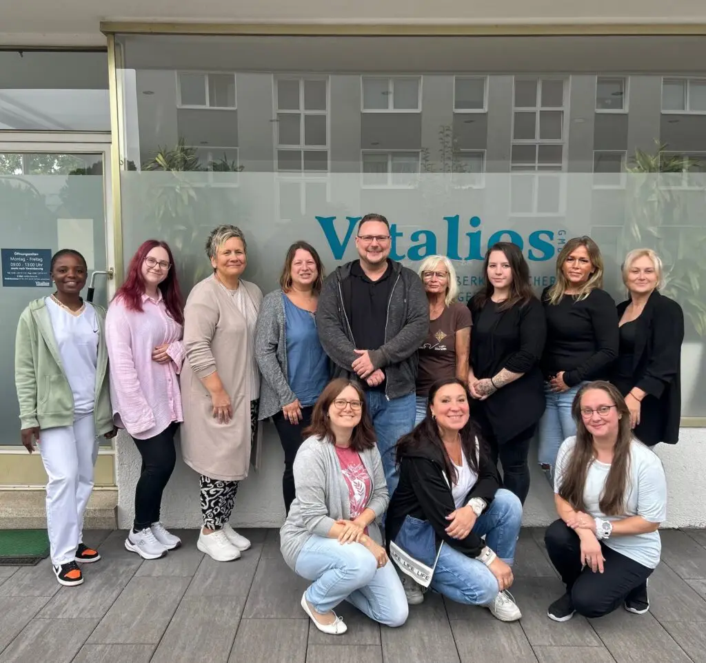 Teamfoto der Vitalios GmbH, Mitarbeiterinnen und Mitarbeiter lächeln vor dem Büro in Mülheim